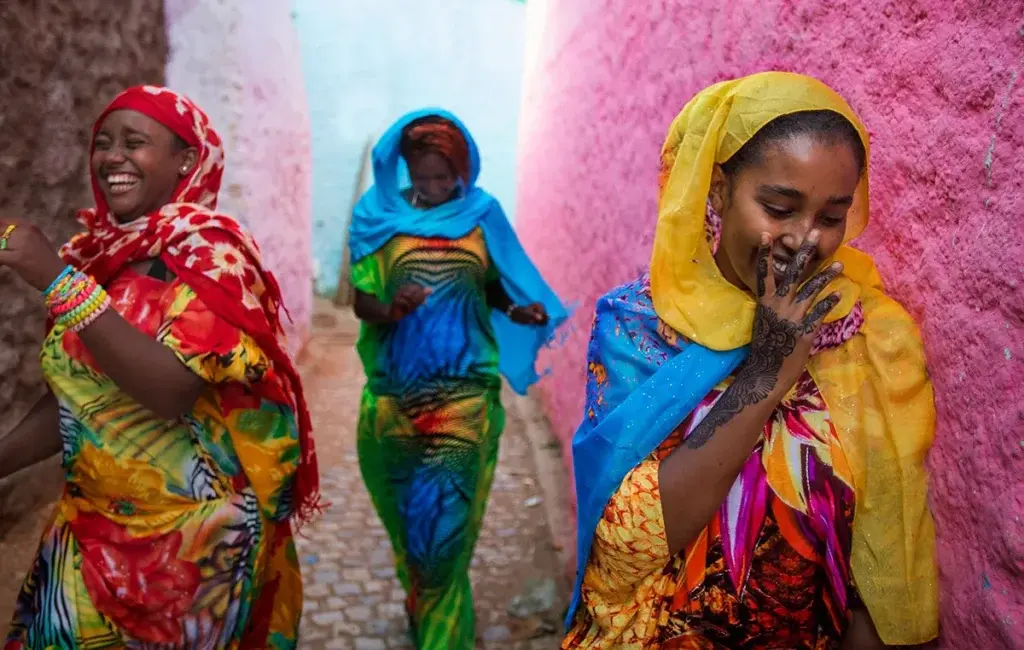Women in colorful dress walking through a pink alleyway in Harar Jugol, Ethiopia